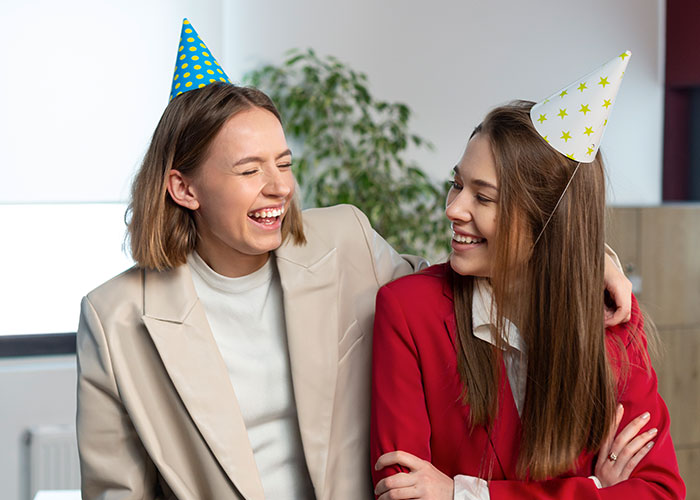 Two women laughing at a party, wearing party hats, celebrating creative marriage hacks.
