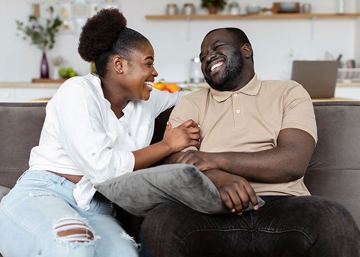 A couple laughing together on a couch, illustrating wild marriage hacks in a cozy home setting.