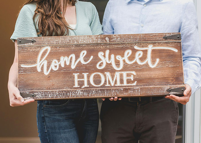 Couple holding rustic "home sweet home" sign, symbolizing marriage harmony and magic hacks.