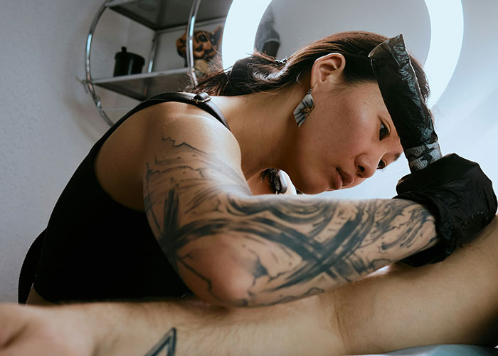 Woman tattoo artist focused on her work, showcasing a way to decenter men by excelling in a traditionally male-dominated field.