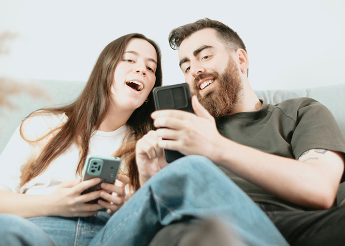 Two people sitting on a couch, smiling and looking at phones, exemplifying ways women decenter men.