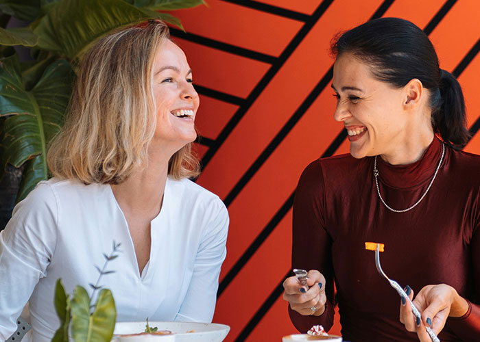 Two women smiling and enjoying a meal together, illustrating ways women decenter men in social settings.