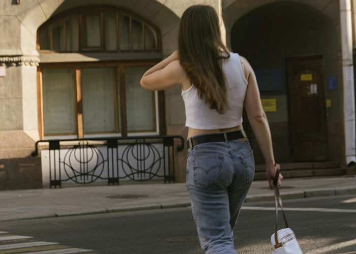 Woman walking on street, wearing jeans and white top, holding a handbag, embodying ways women "decenter" men.