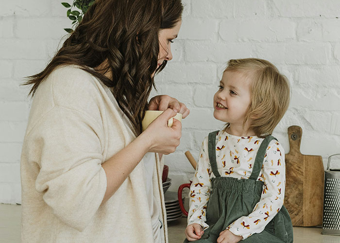 Woman holding a mug, smiling at a child in a cozy kitchen setting, showcasing ways women decenter men.