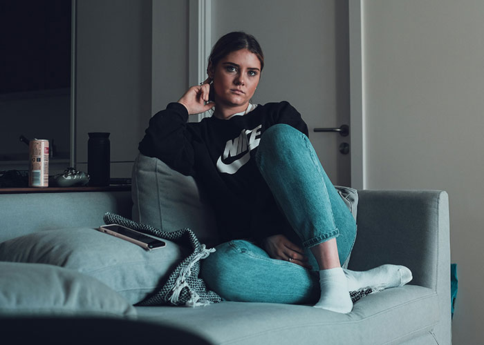 Woman lounging on a sofa, wearing a black Nike sweatshirt and jeans, exemplifying ways women decenter men in daily life.