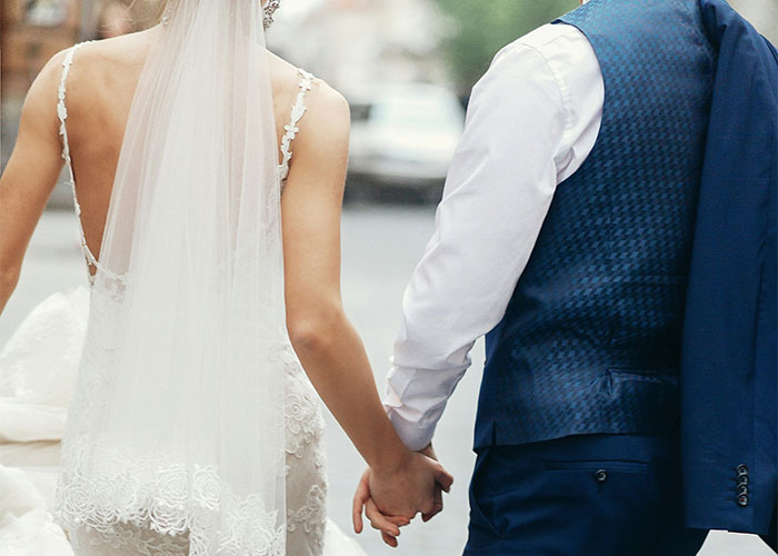Bride and groom holding hands, back view, showcasing decentering men.