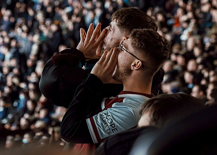 Fans in a stadium cheering passionately during a game, engaging with the crowd around them.