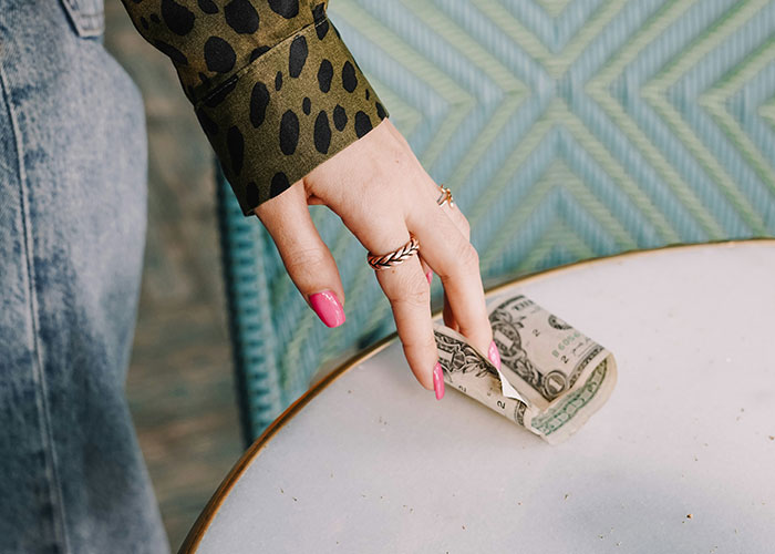 Woman's hand with pink nails placing money on a table, illustrating ways women "decenter" men.