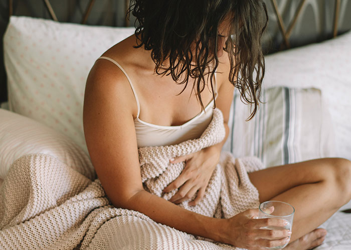 Woman sitting on a bed with a blanket and a glass, embodying ways women decenter men in daily life.
