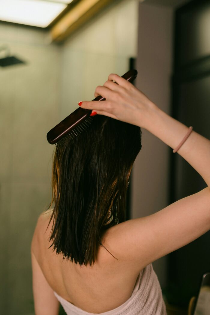 Woman combing wet hair in bathroom, unhinged coworker stress reliever.