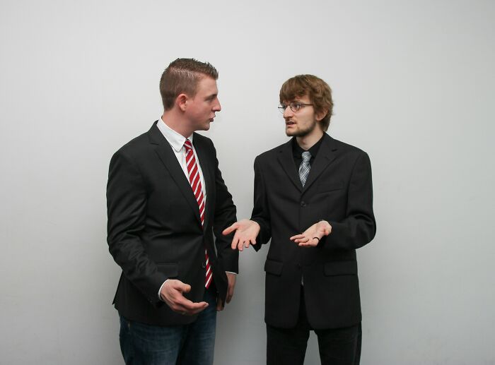 Two coworkers in suits having an intense discussion against a plain background.