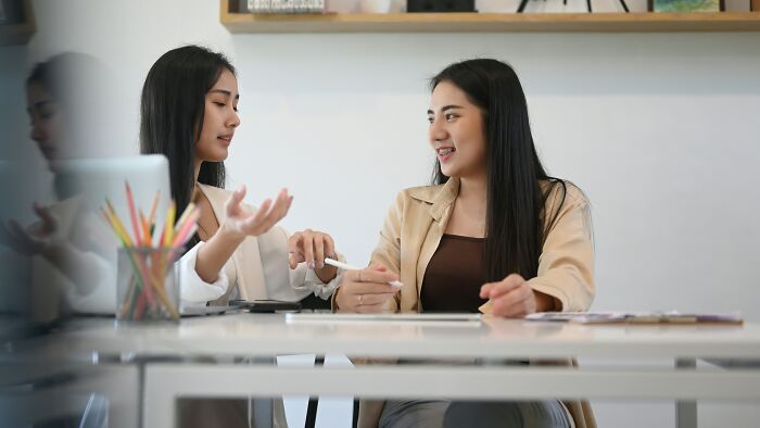 Two coworkers discussing strategies at a desk, sharing ideas on dealing with coworkers you can't stand.