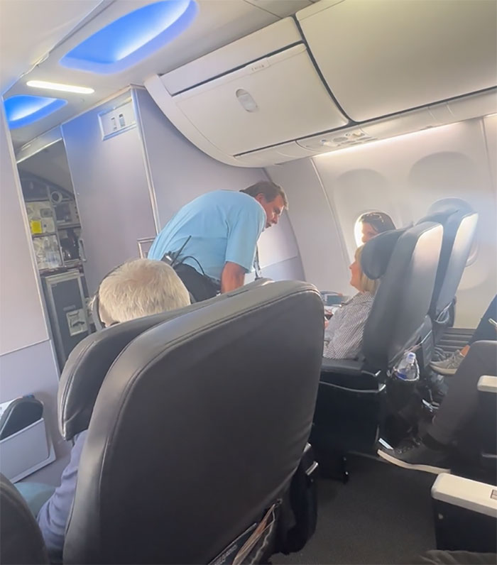 Flight attendant in blue shirt talking to passengers in plane cabin, related to incident with disabled woman seeking help. Flight attendant in blue shirt talking to passengers in plane cabin, related to incident with disabled woman seeking help.