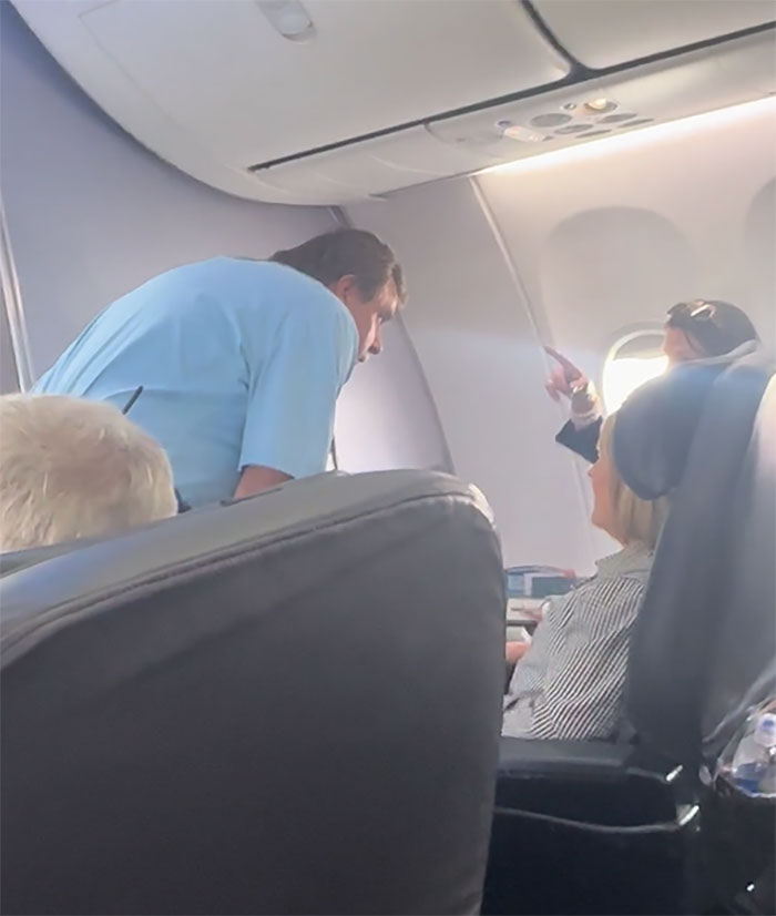 Flight attendant and passengers in discussion onboard, with focus on a seated woman, highlighting airline incident. Flight attendant and passengers in discussion onboard, with focus on a seated woman, highlighting airline incident.