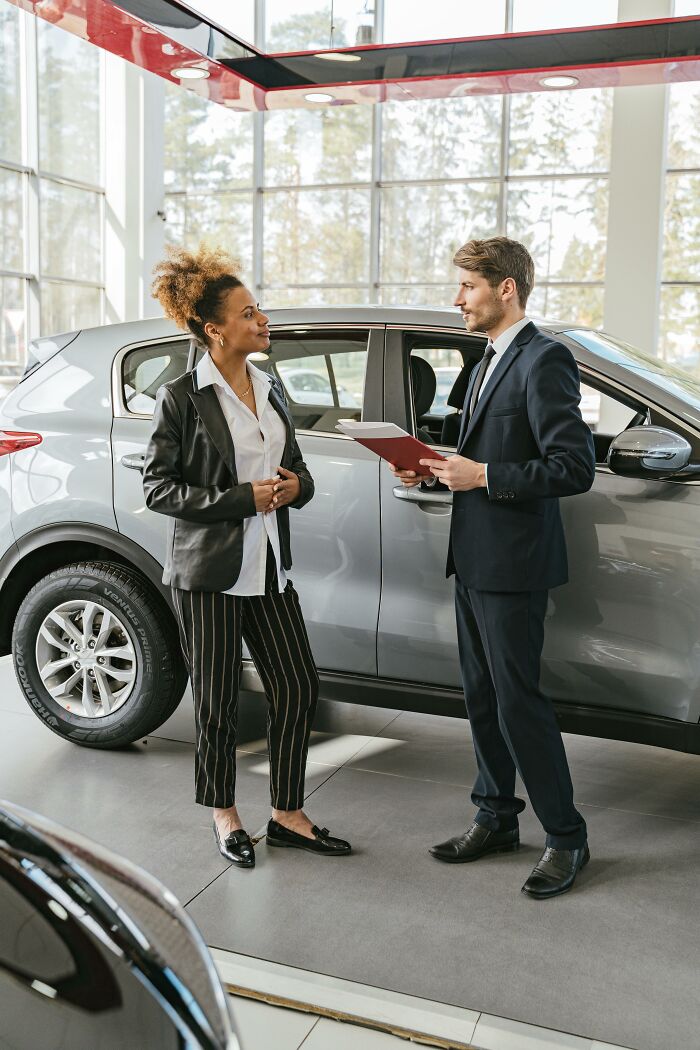 Two people discussing a car purchase in a showroom, relating to expensive weddings.