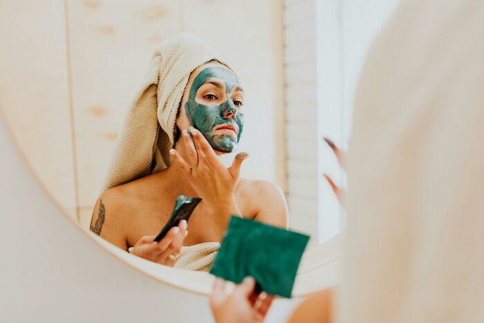 Person in towel applying face mask in mirror, preparing for an expensive wedding.