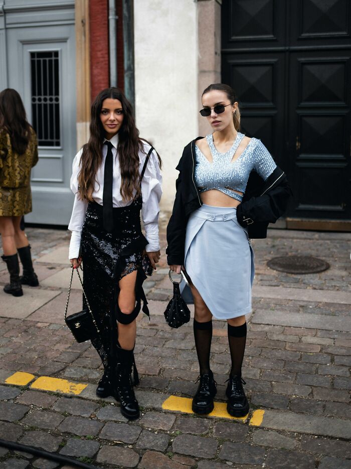Two fashionable women in trendy outfits posing on a cobblestone street, embodying expensive weddings style.