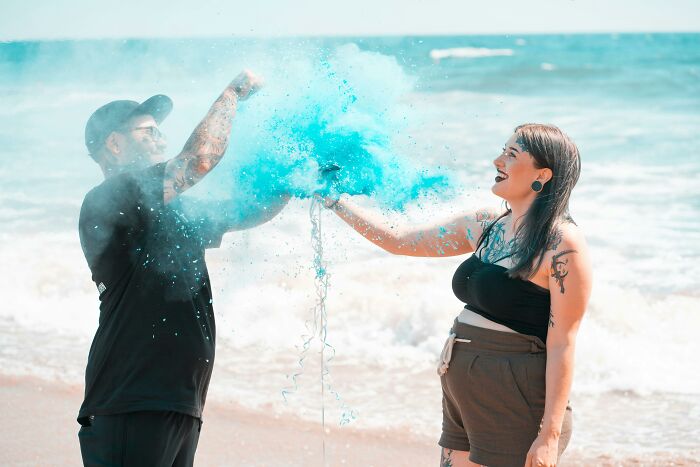Couple celebrating with blue powder on the beach, reflecting expensive weddings trend in vibrant outdoor setting.