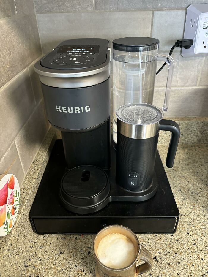 Keurig coffee maker on a kitchen counter with a frothy cup, highlighting expensive weddings and lifestyle choices.
