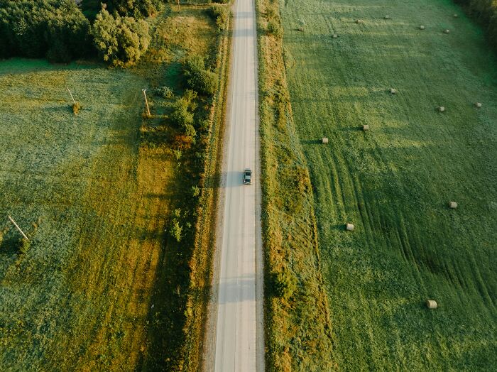 Aerial view of a car driving down a long road through green fields, symbolizing journey with absolute confidence.