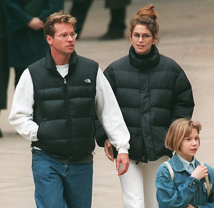 Man in casual attire walking with two women, wearing winter coats, in an urban setting.