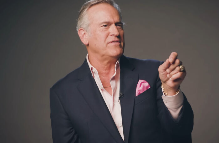 Elderly man in suit gesturing, embodying a friendly celebrity vibe.