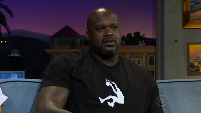 Celebrity on a talk show set, wearing a black shirt with a white graphic, discussing fan experiences.