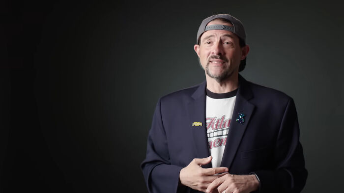 A celebrity in a casual outfit and cap, gesturing while speaking on stage.