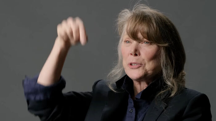 A person gestures enthusiastically, wearing a black suit and navy shirt, discussing their experience with a nice celebrity.