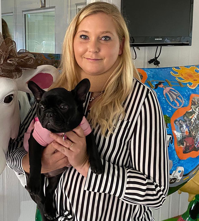 Woman in a striped shirt holding a black dog, next to a decorative cow, related to Prince Andrew's accuser news.