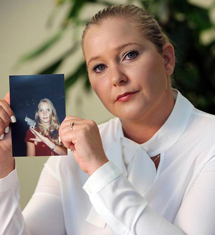 Woman holding a photo, linked to Prince Andrew in legal case, looking serious while seated indoors.