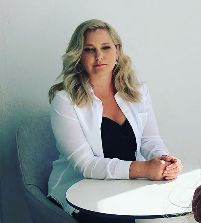 Woman with blonde hair, wearing a white shirt over black top, sitting at a round table, discussing Virginia Giuffre lawyer claim doubt.