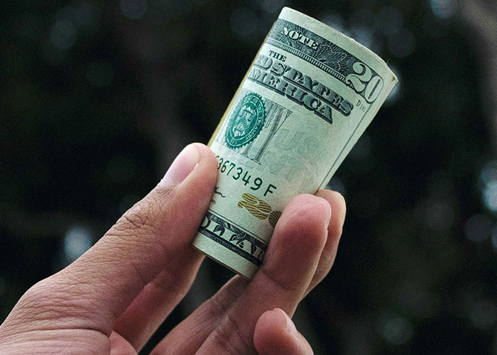 Hand holding rolled cash, representing tipping in service industry.