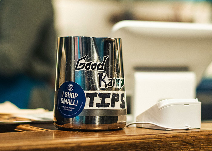 Tip jar labeled "Good Karma" on a counter, next to a "Shop Small" sticker.