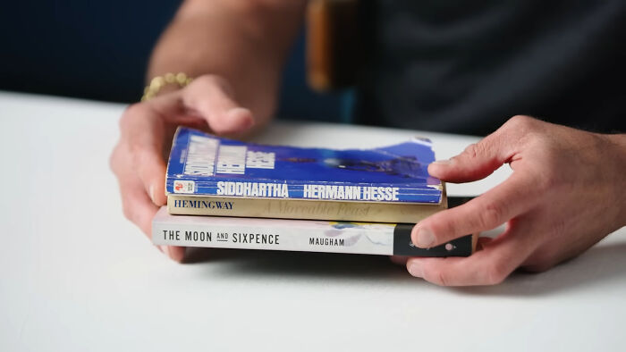 Hands holding a stack of books, including Siddhartha by Hermann Hesse, showcasing Walton Goggins' essential items.