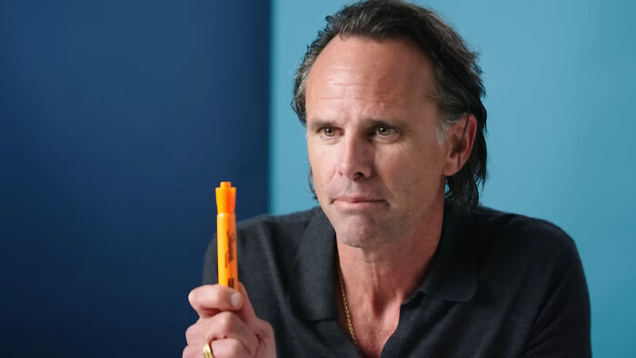Man holding an orange marker in a blue-walled room, discussing essential things.