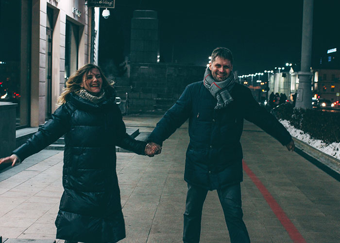 A smiling couple in winter coats walking at night, illustrating intuition to leave a situation.