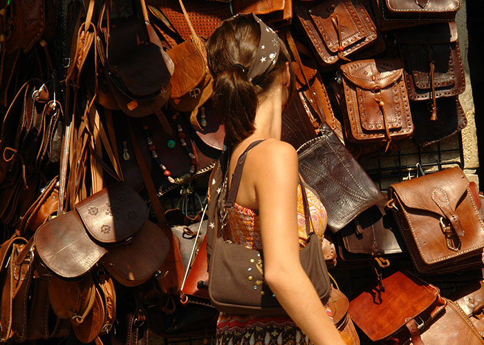 Woman shopping for leather bags at an outdoor market, showcasing intuition in choosing quality craftsmanship.