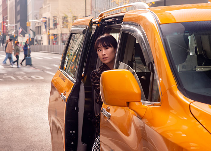 Mujer en taxi amarillo mirando hacia afuera en una calle urbana, experimentando un momento decisivo para irse.