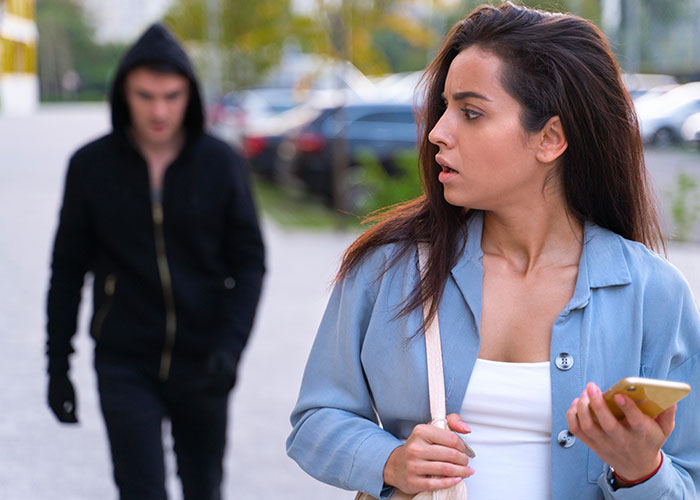 Woman sensing intuition to leave as hooded figure follows on street, holding a phone.