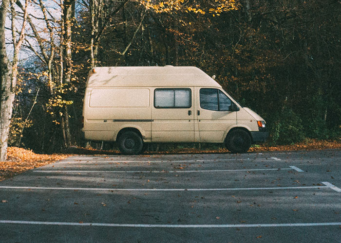 Beige van parked in a deserted wooded area, surrounded by autumn leaves, hinting at an intuitive decision to leave.