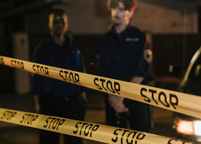 Cinta de advertencia amarilla con "STOP" y dos personas uniformadas de fondo en un área oscura, representando experiencias salvajes.