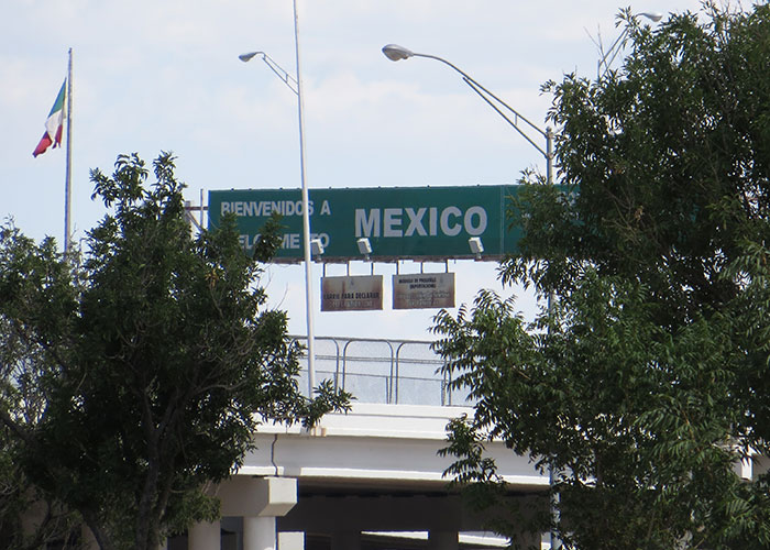 Letrero de bienvenida en frontera México, entre árboles, con cielo despejado. Experiencia relacionada con desplazarse.