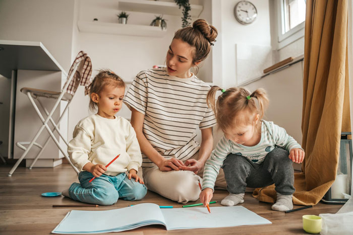 Teen babysitter in a striped shirt with two kids on the floor, coloring together in a cozy room. Teen babysitter in a striped shirt with two kids on the floor, coloring together in a cozy room.