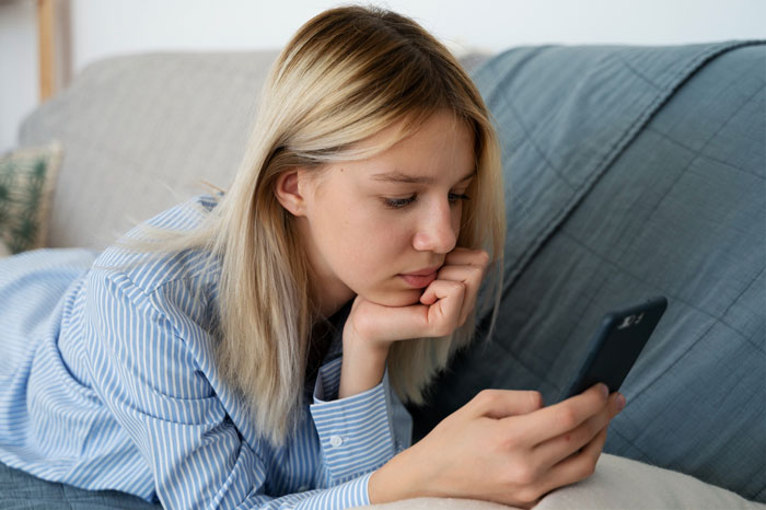 Teen upset after babysitting dispute, looking at her phone while resting on a couch. Teen upset after babysitting dispute, looking at her phone while resting on a couch.