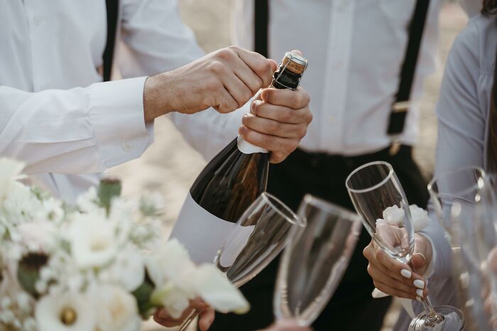 Hands opening champagne at a wedding, surrounded by flowers and glasses, depicting celebration and joy. Hands opening champagne at a wedding, surrounded by flowers and glasses, depicting celebration and joy.
