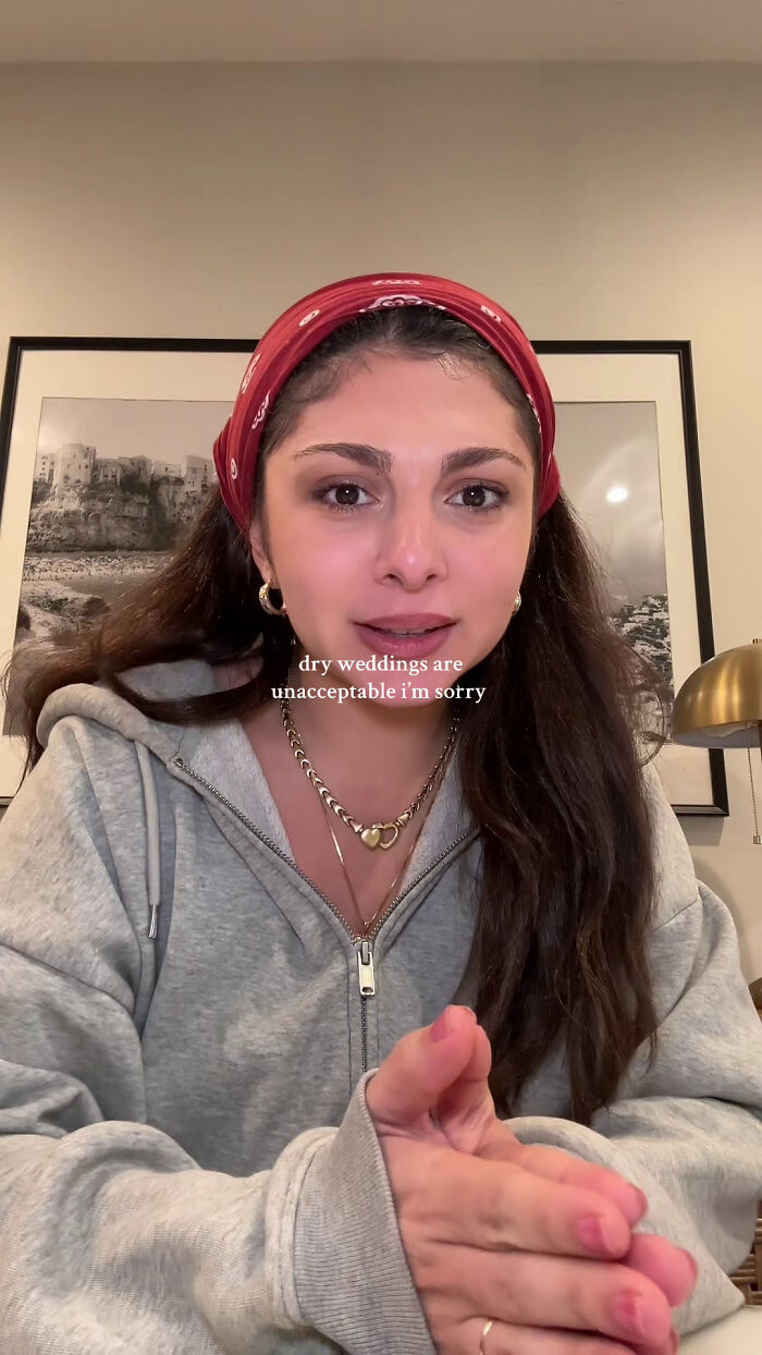 Woman discusses dry weddings, wearing a red headband and gray hoodie with framed picture background. Woman discusses dry weddings, wearing a red headband and gray hoodie with framed picture background.