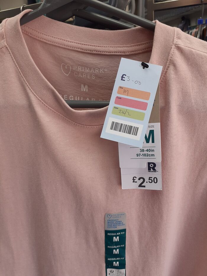Pink T-shirt in a secondhand shop with multiple price tags, one showing £3.00 and another £2.50.