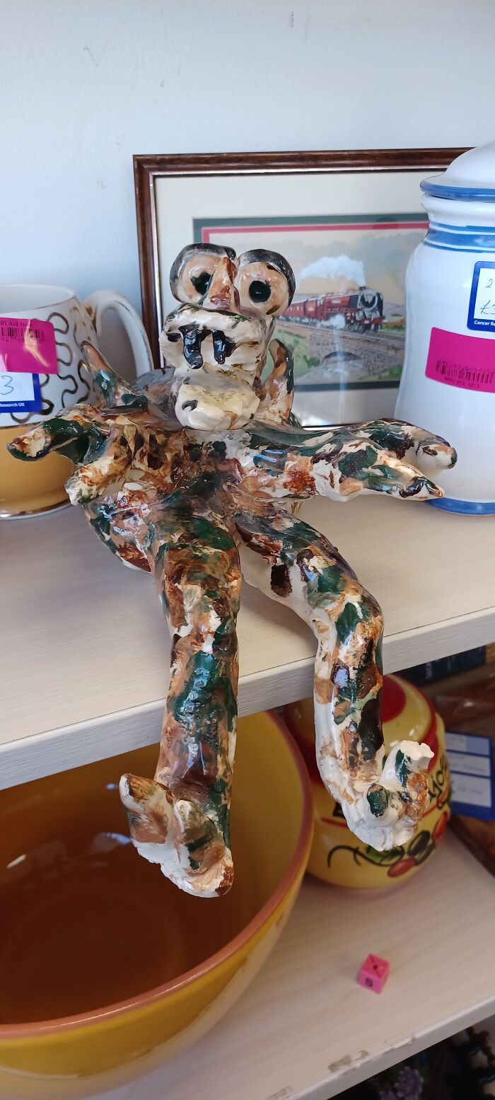 Bizarre ceramic creature found in a secondhand shop, surrounded by various pottery items on a shelf.
