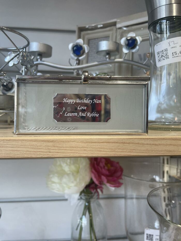 Silver box with a personalized birthday message inside a secondhand shop, surrounded by glassware and flowers.